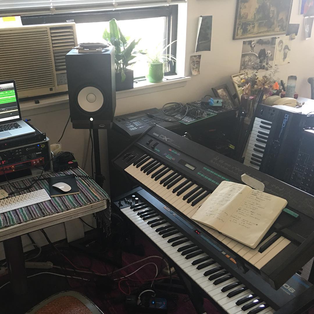 Home studio setup from 2016 featuring a Yamaha DX7 and Roland Juno-106 synthesizer in the foreground, with a Roland D-50 and Dave Smith Instruments Prophet ’08 stacked behind them. Several drum machines and desktop synths sit to the left, including a Roland R-8, Roland TR-8, and Elektron Analog Four.