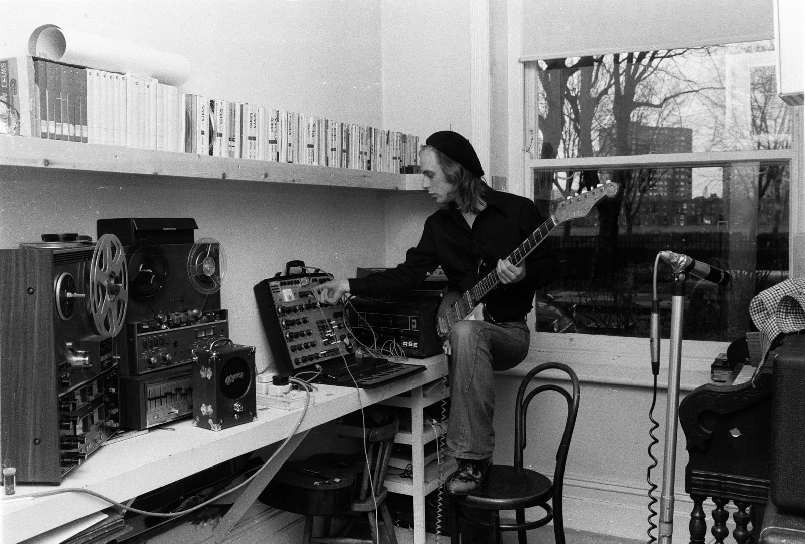 Brian Eno in his studio in 1974. On his desk are two tape machines and a Synthi A synthesizer.